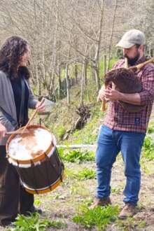 Mulher e homem tocam bombo e gaita de foles no meio da natureza